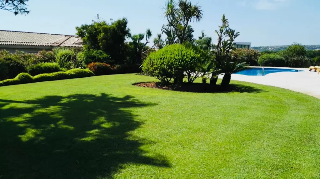 Jardín con pradera de césped natural, setos y piscina en una villa de Sotogrande